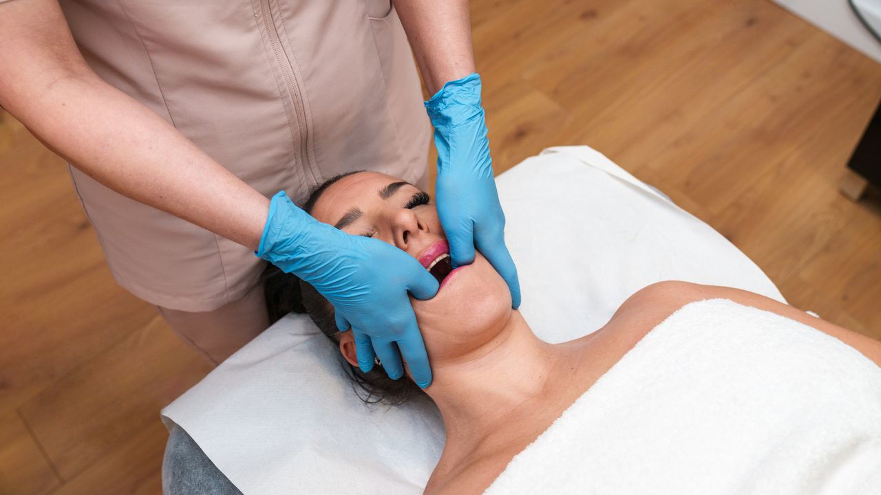 Behandlerin tastet mit Handschuhen die Kaumuskulatur einer liegenden Patientin ab