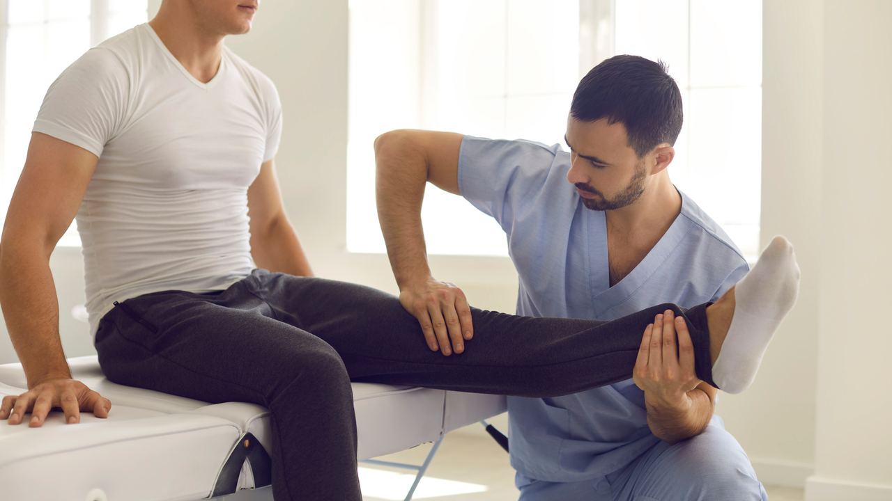 Therapeut hebt und dehnt das gestreckte Bein eines sitzenden Sportlers
