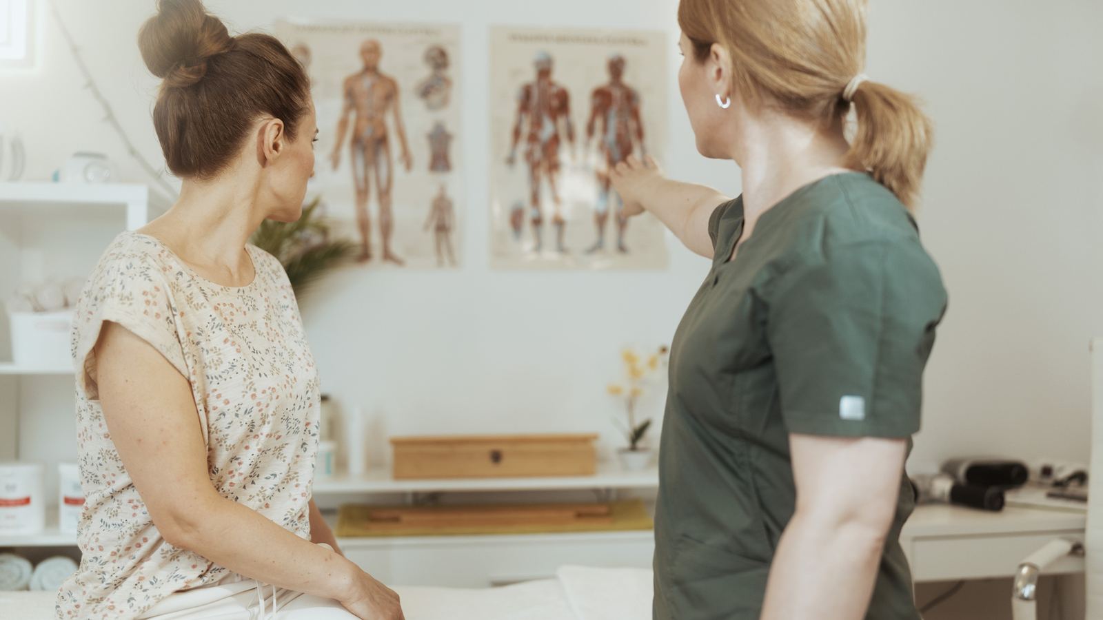 Therapeutin erklärt einer zweiten Person etwas am anatomischen Plan an der Wand